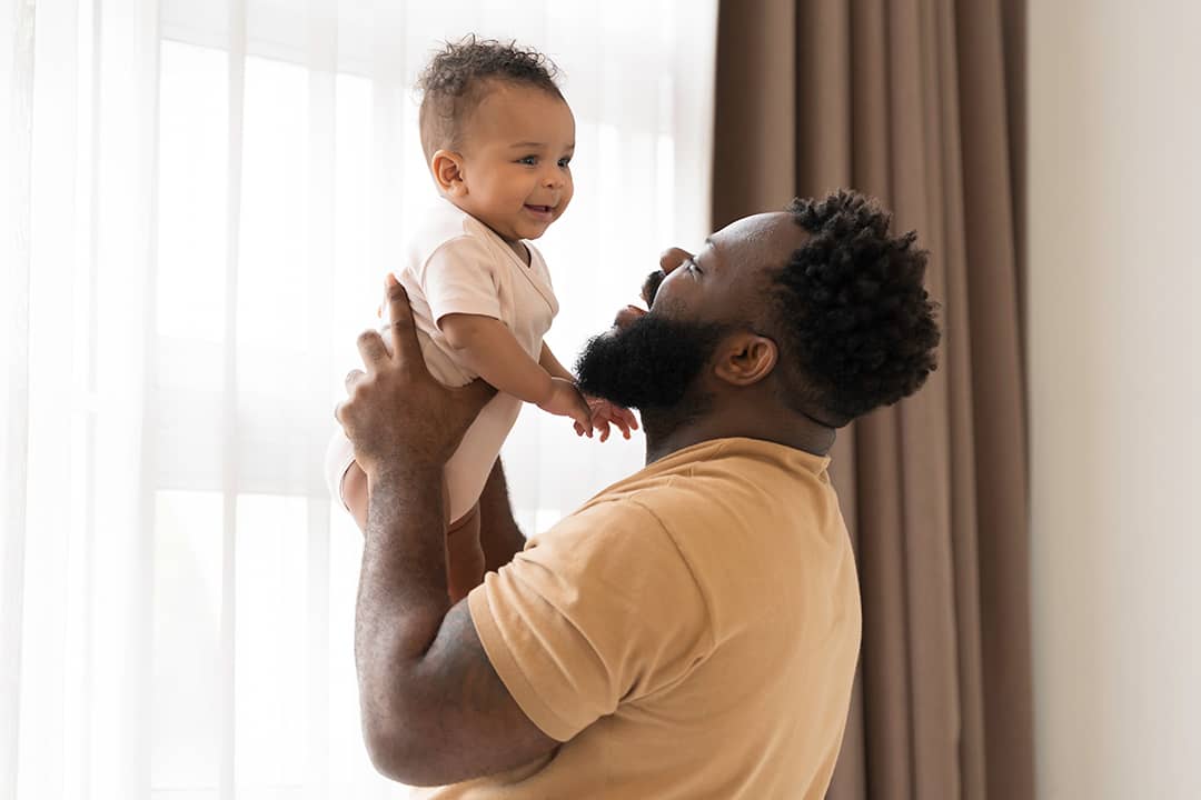 A father happily carrying his baby in the bedroom.